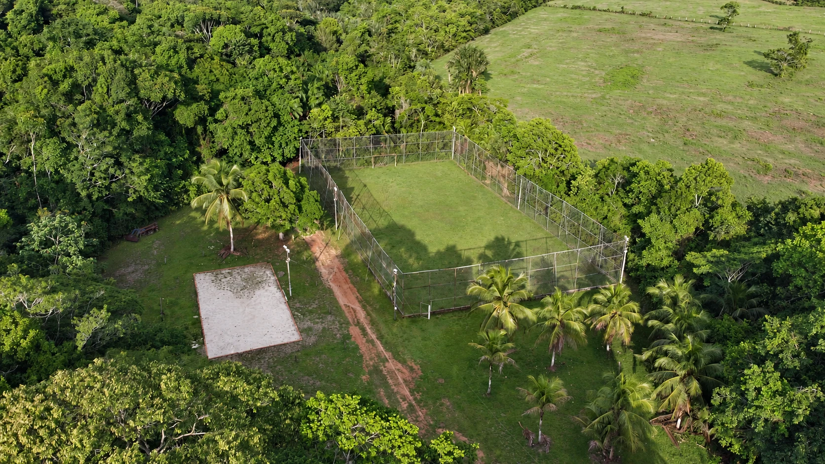 Vista aérea da quadra de futebol e da quadra de areia cercadas pela mata