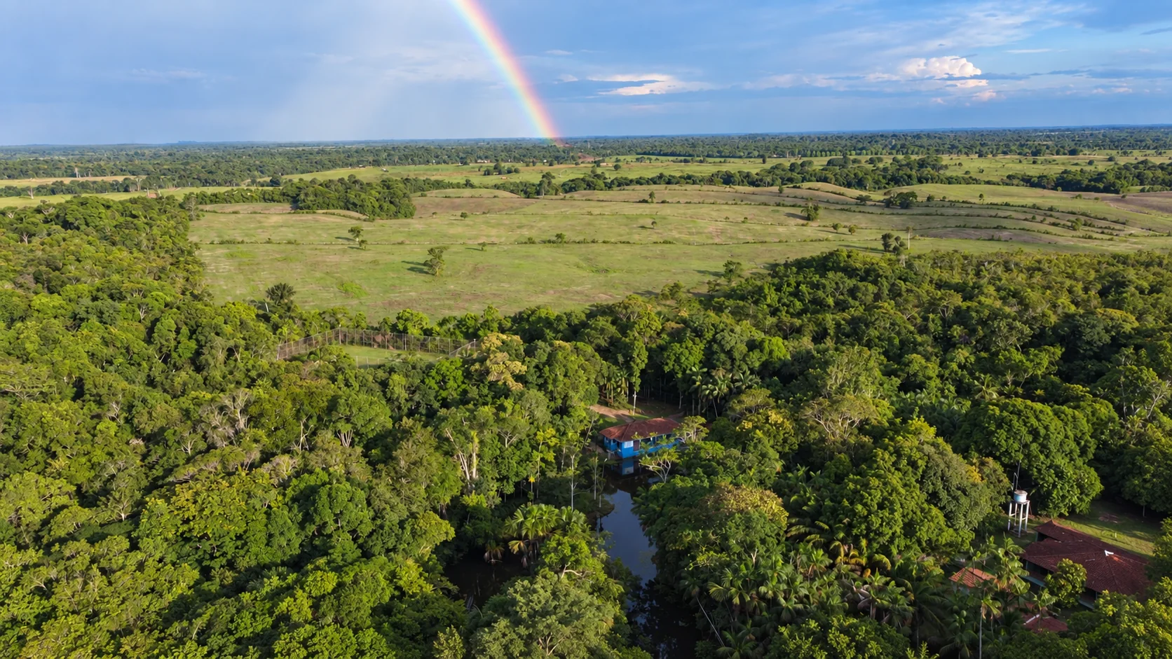 Paisagem aérea do Recanto cercado de vegetação sob um arco-íris